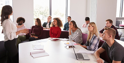 White female teacher in front of a classroom of  young adult students of various races